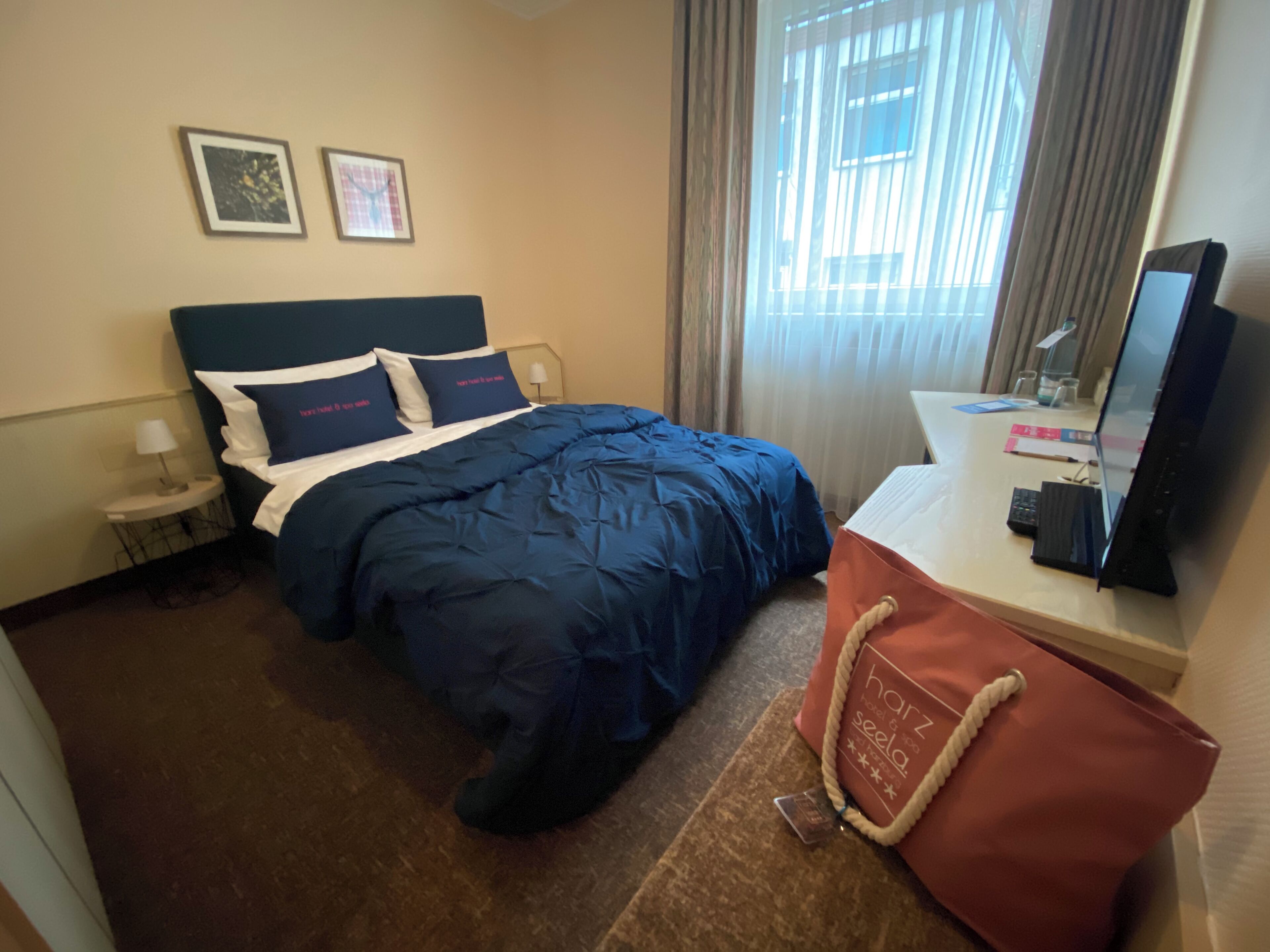 A hotel room with a bed, a desk with a computer, a lamp, and a handbag on the desk.