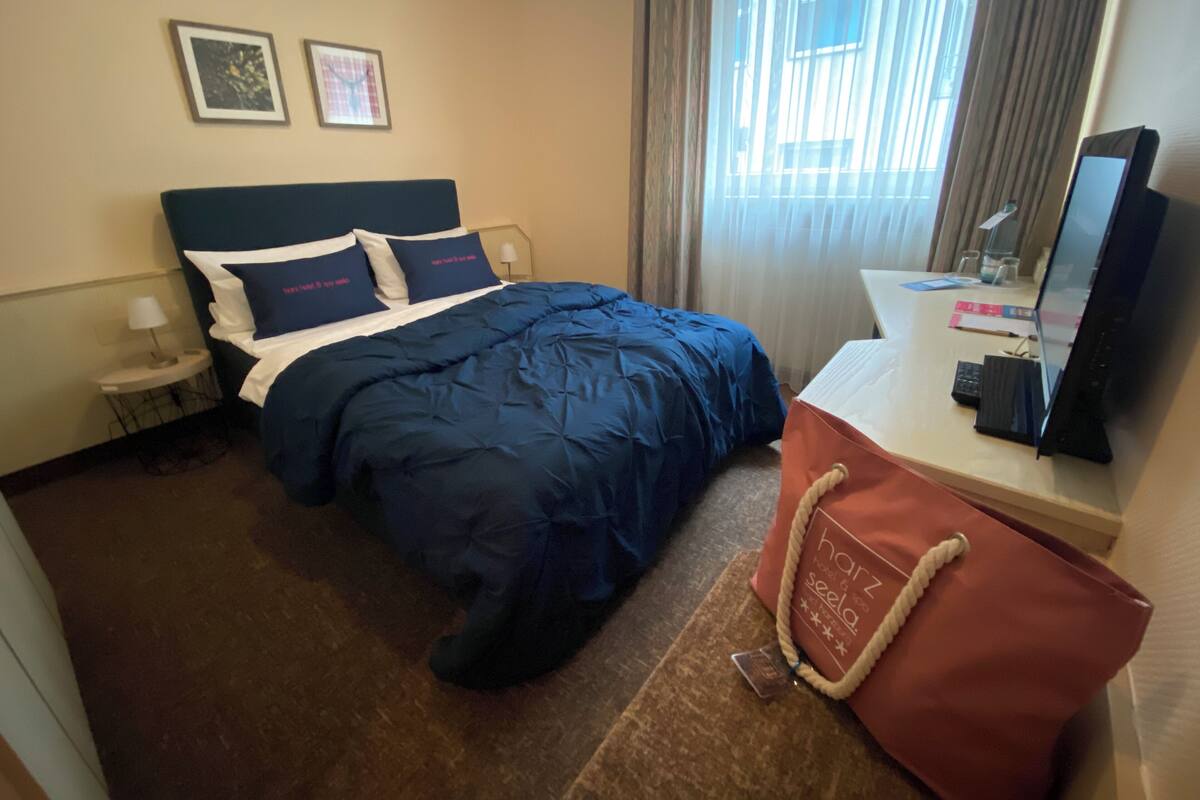 A hotel room with a bed, a desk with a computer, a lamp, and a handbag on the desk.