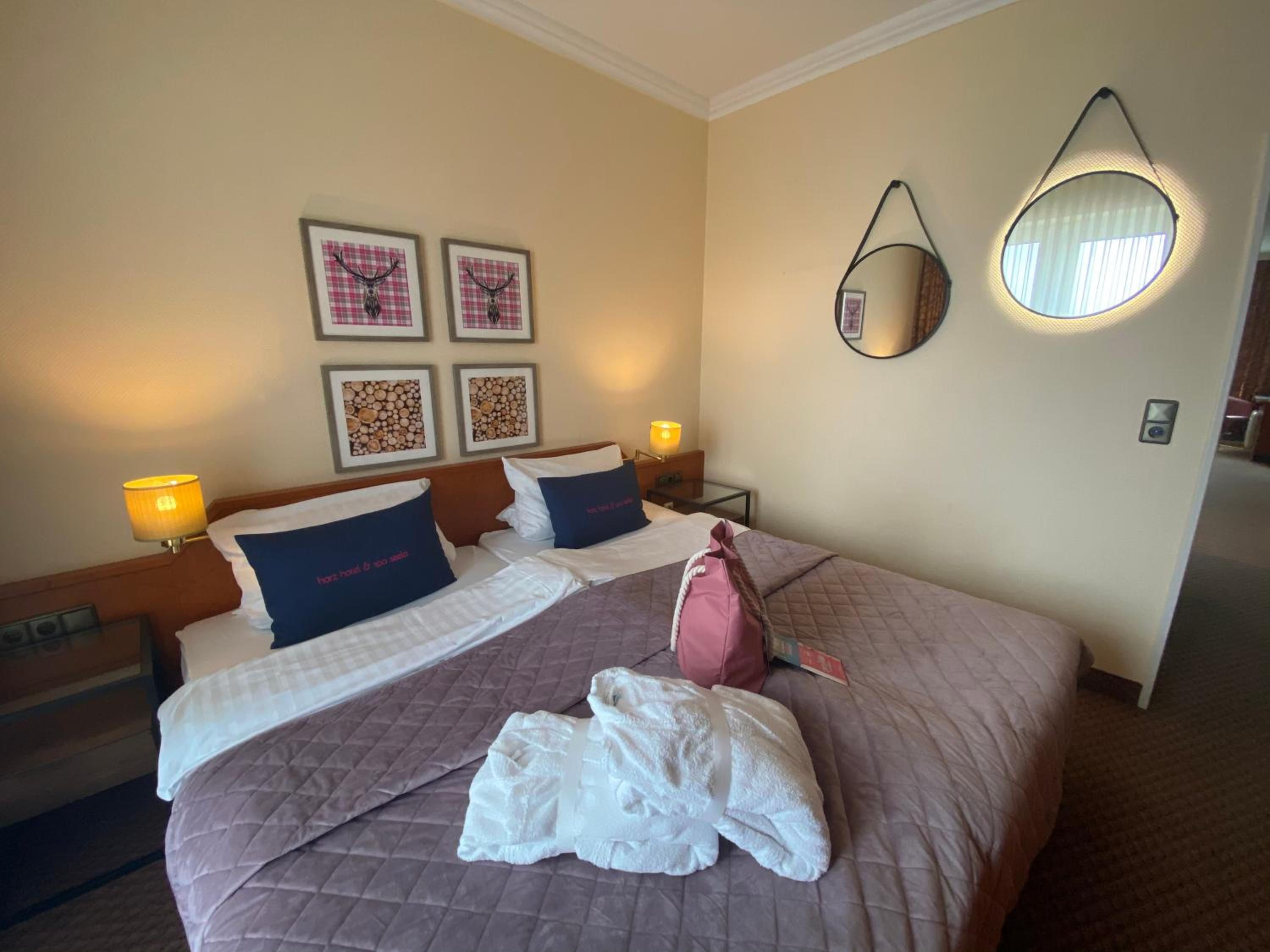 Una habitación de hotel con una cama, dos lámparas de noche, un espejo montado en la pared y obras de arte enmarcadas.
