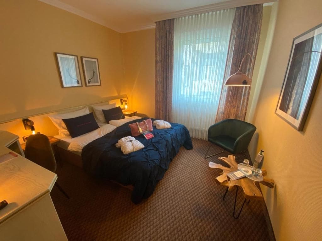 Een hotelkamer met een bed, nachtkastje, lamp, stoel en een raam met gordijnen.