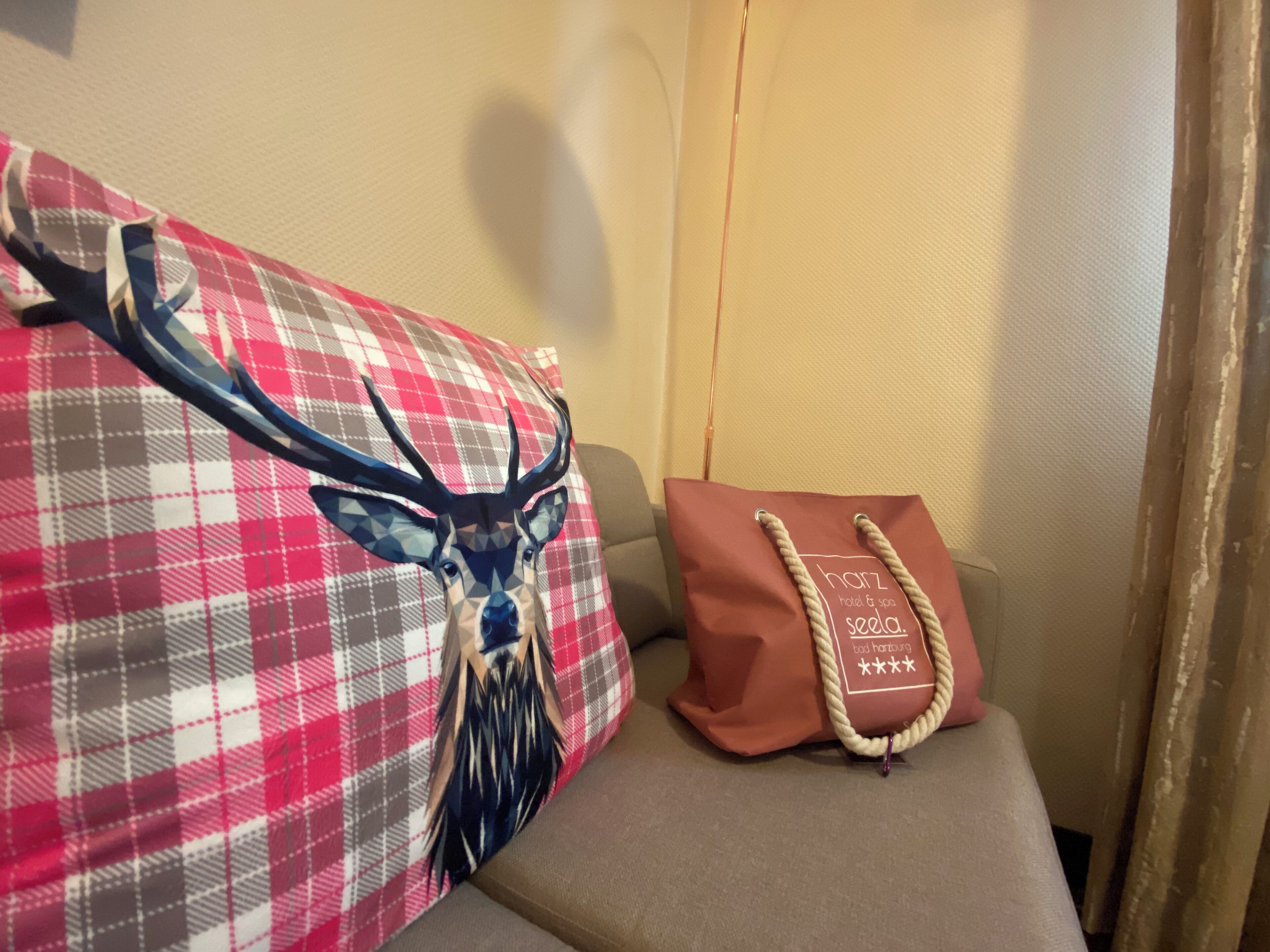 Una habitación con un cojín de cuadros con diseño de cabeza de ciervo, un cojín marrón con asa de cuerda y una pared color beige.