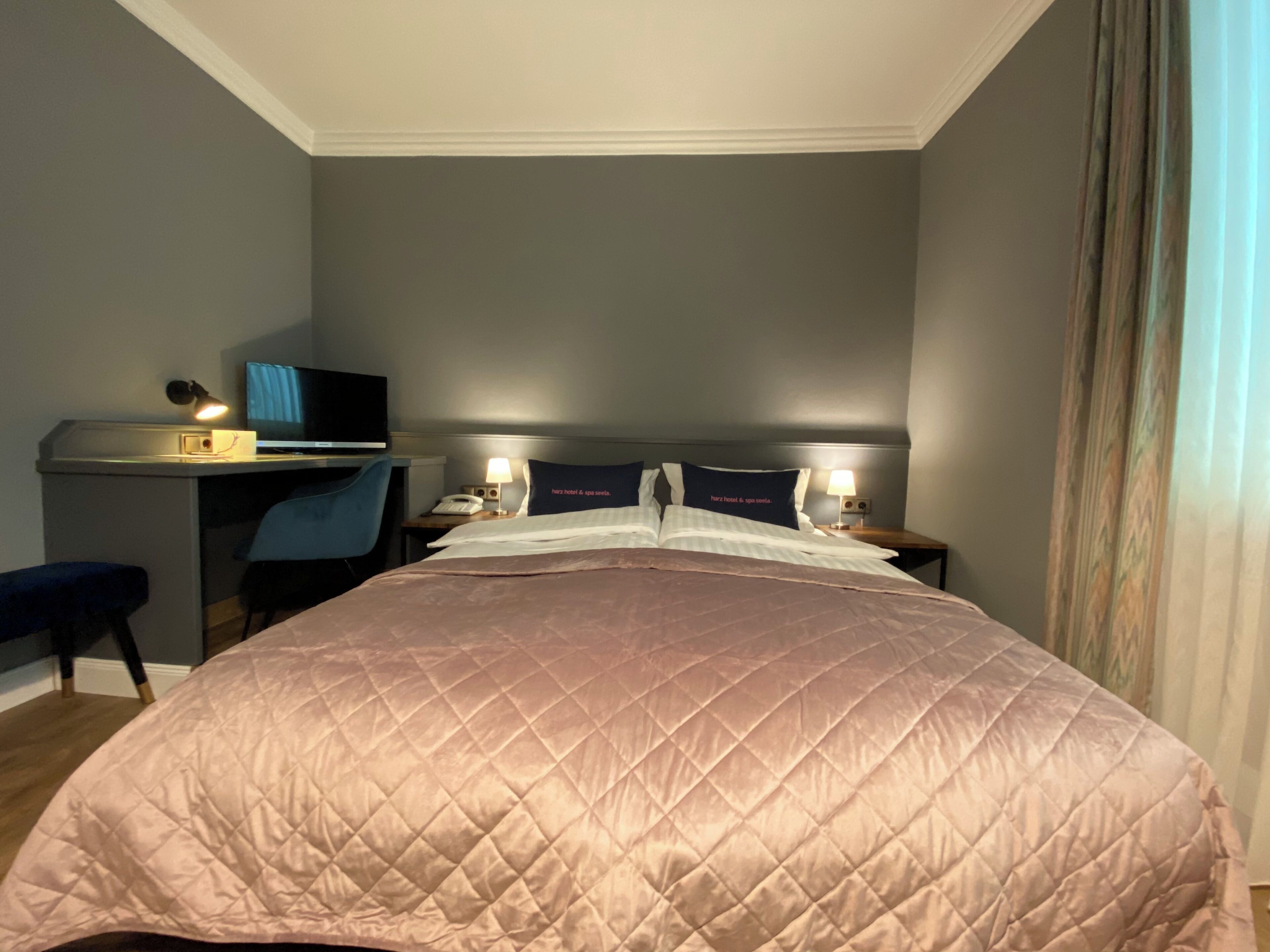 Habitación de hotel con una cama grande, un escritorio con computadora, una silla y dos lámparas de noche.