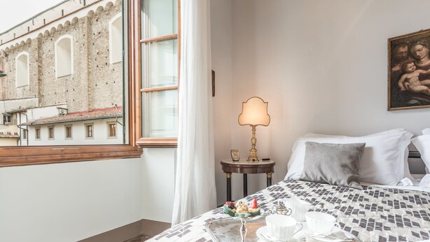 Habitación de hotel con una cama, una bandeja con tazas, un atril para bandeja, una lámpara y un cuadro en la pared.