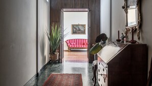 Un pasillo con piso de madera, una planta en maceta, un sofá a rayas rojo y blanco, y un aparador de madera con espejo.