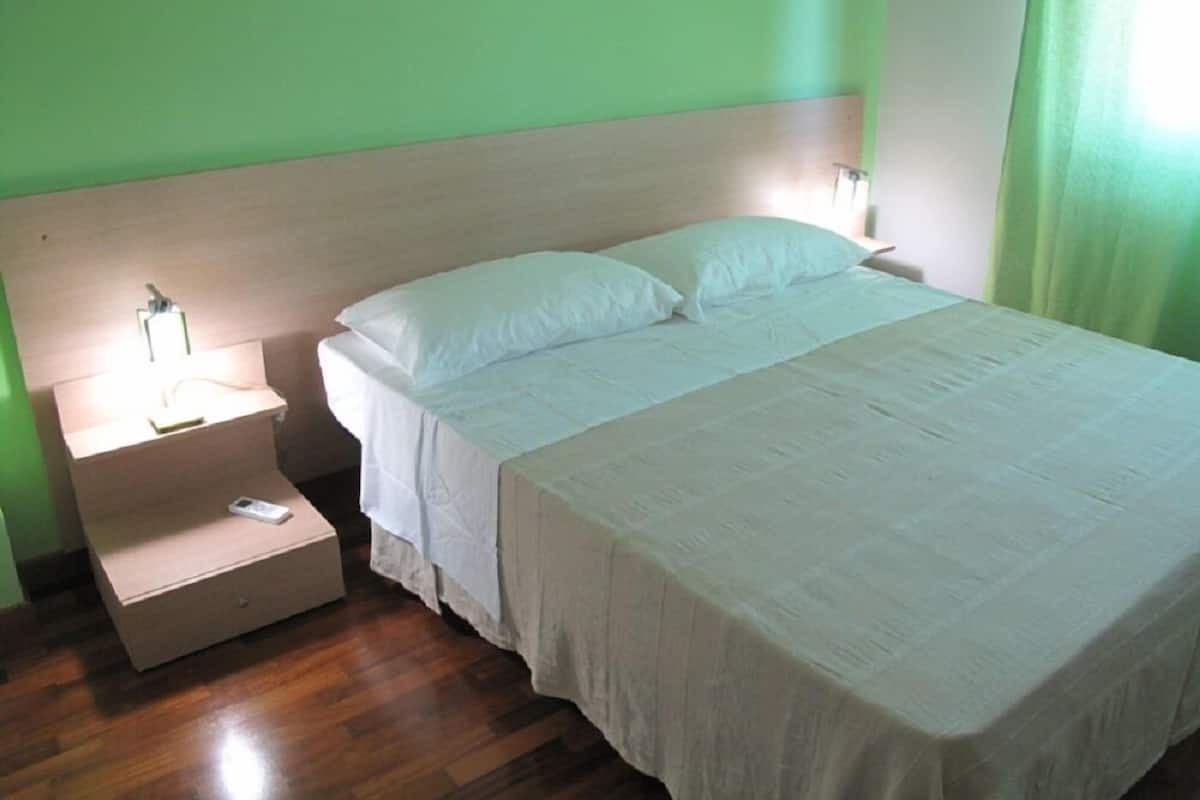 A neatly made bed with white linens in a room with green walls and wooden flooring.