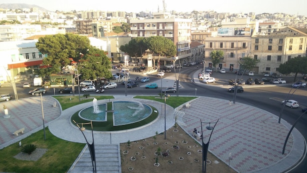 A public square with a fountain, surrounded by trees and benches, with buildings in the background. - B&B Santa Caterina (Reggio Calabria)