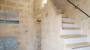 Una habitación con paredes de piedra, un sofá estampado, una escalera con escalones blancos y un cuadro de una playa.