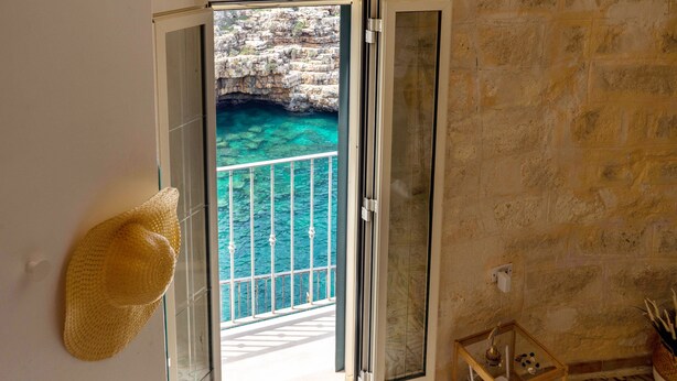 Una habitación con vista a un litoral rocoso y agua azul cristalina a través de un ventanal.