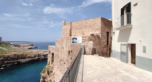 A stone building with a balcony overlooking a coastal area. - Sogno Blu (Polignano a Mare)