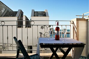En balkon med et bord, en stol og en flaske vin.