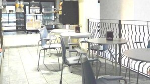 Un restaurante con varias mesas y sillas, una zona de cocina al fondo y una persona a lo lejos.