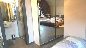 Una habitación de hotel moderna con un espejo grande, una cama con colcha de rayas azules y blancas, y suelo de madera.