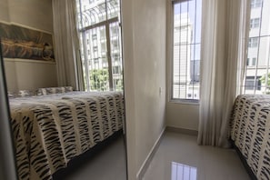 A bedroom with two beds, large windows, and a painting on the wall.
