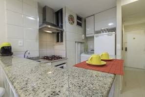 Cozinha com bancadas de granito, fogão a gás, coifa em aço inoxidável e geladeira branca.