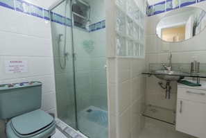A bathroom with a glass shower enclosure, a toilet with a colorful seat cover, and a sink with a mirror above it.