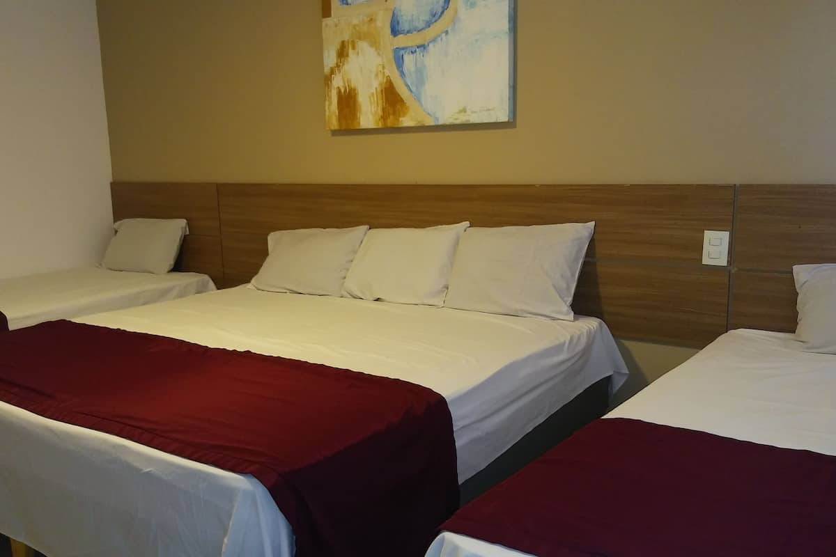 Quarto de hotel com duas camas de solteiro e uma cama de casal, todas com roupa de cama branca e colchas vermelhas.