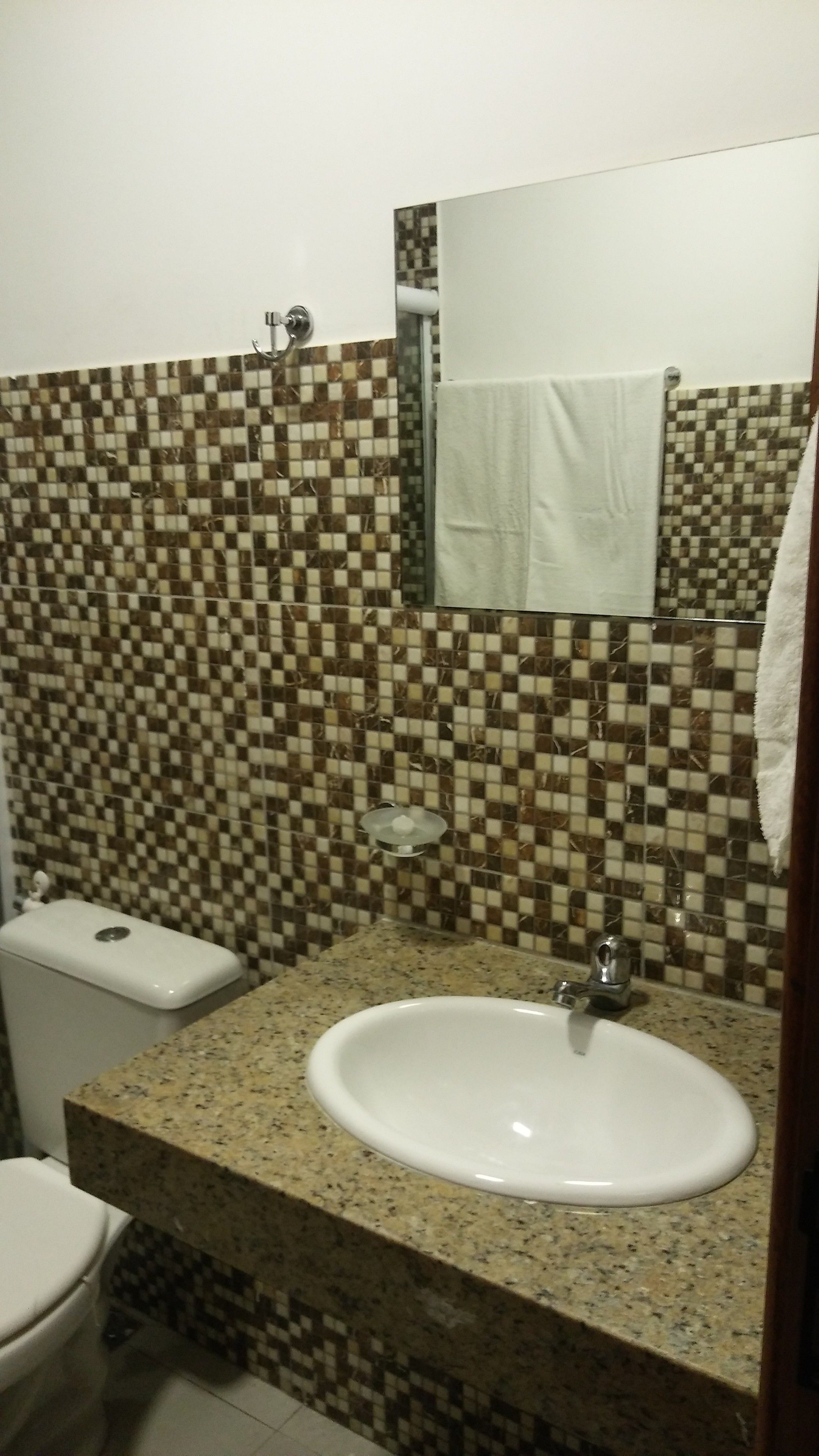 A bathroom with a checkered tile backsplash, a white sink, and a toilet.