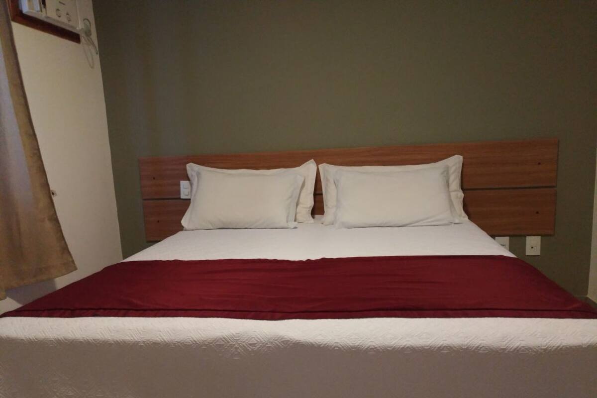 Uma cama com cabeceira de madeira, roupa de cama branca e um cobertor vermelho.
