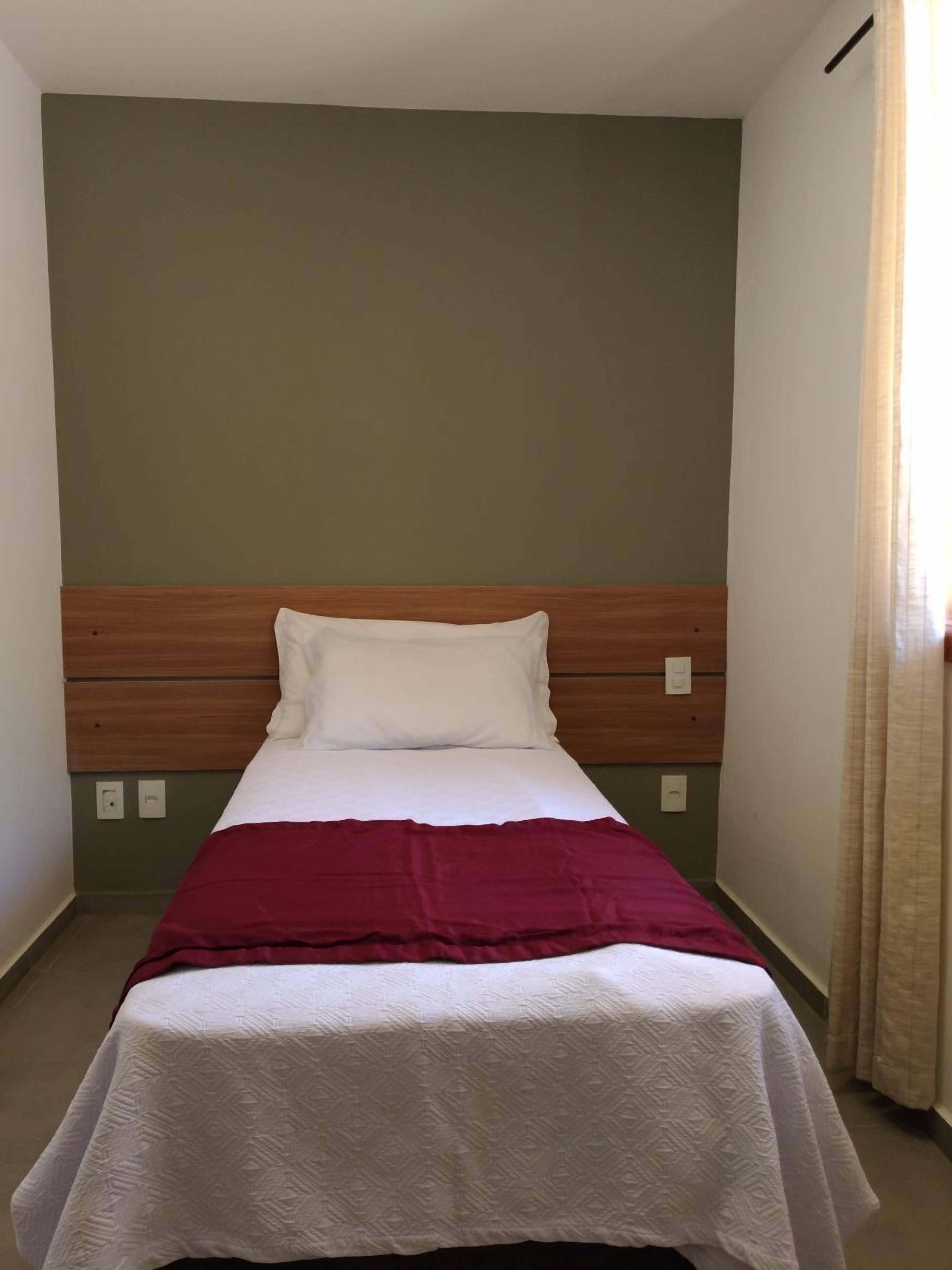 Een enkel bed met een houten hoofdbord, witte beddengoed en een rode deken.