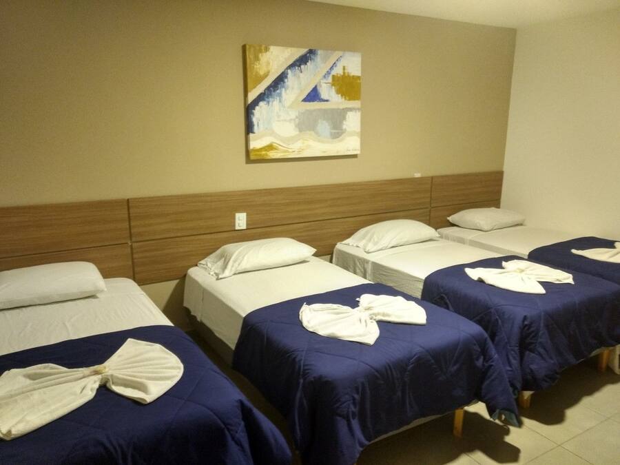A hotel room with four single beds, each with a blue bedspread and white pillows. There is a painting on the wall above the beds.