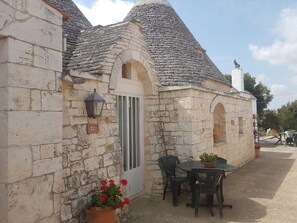 A stone building with a tiled roof, a door, and a small table with chairs outside. - Masseria Gianca (Cisternino)