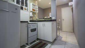 Uma cozinha compacta com geladeira branca, fogão Electrolux e micro-ondas em cima. Há armários com painel de azulejos e uma pequena prateleira acima da pia.