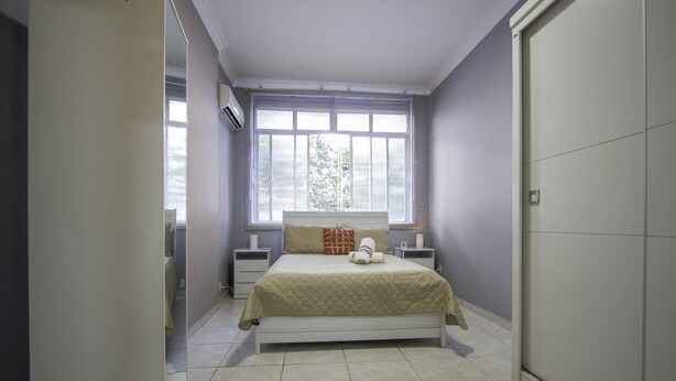 Um quarto com cama, mesas de cabeceira, uma janela e uma porta.