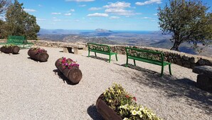 A scenic outdoor seating area with stone benches and planters, overlooking a mountainous landscape. - Terry's House (Nuoro)