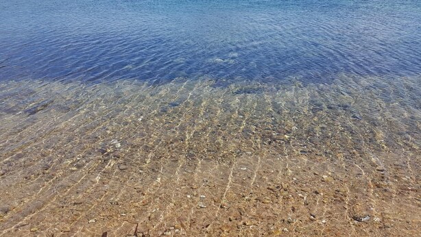 A clear beach with visible pebbles and a distant mountain. - Terry's House (Nuoro)