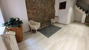 A room with a stone wall, a wooden floor, a chair, a small table, and a staircase. - Terry's House (Nuoro)