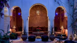 A cozy lounge area with a sofa, two armchairs, a coffee table, and potted plants. - Riad Meriem (Marrakech)