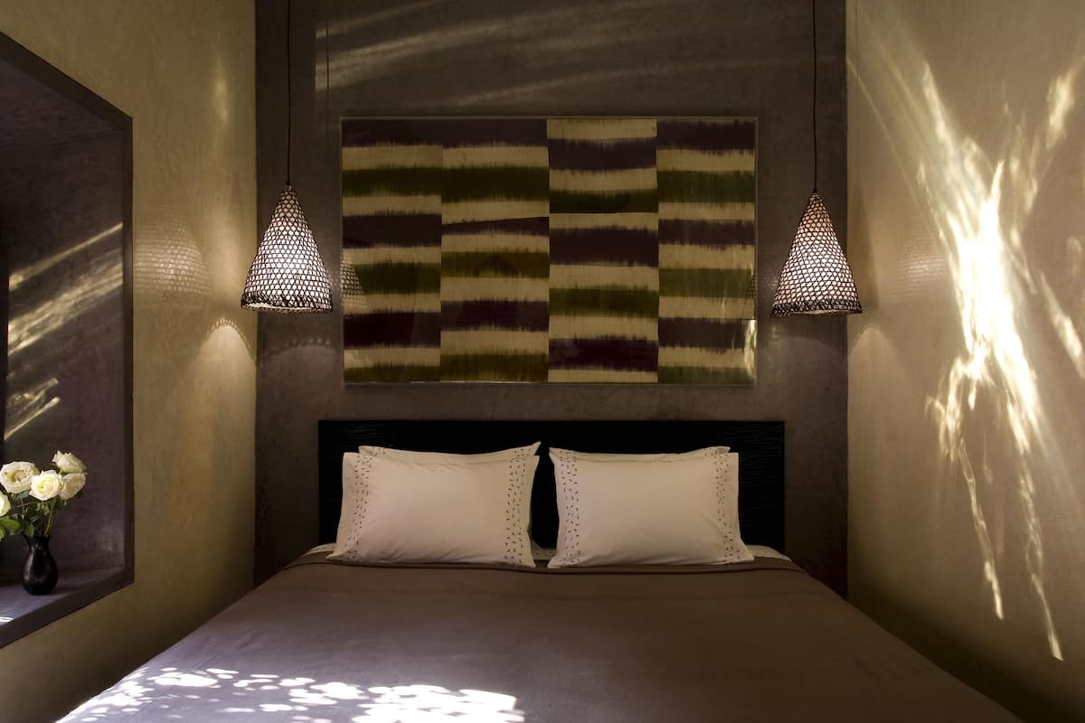 A neatly made bed with two pillows, a wall-mounted artwork, and two hanging lamps.