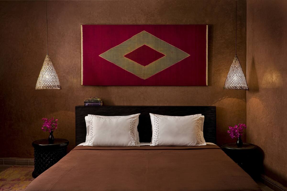 A hotel room with a large bed, two nightstands, a red accent wall, and two pendant lights.