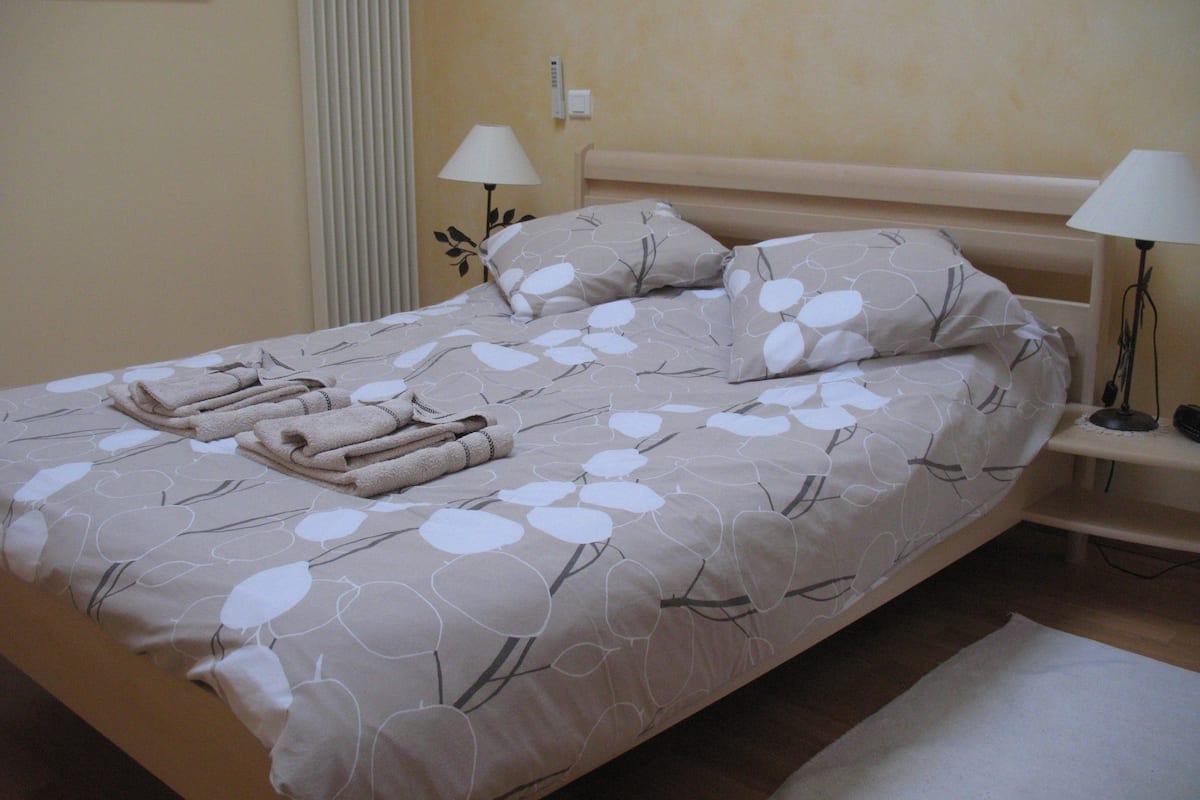 A neatly made bed with a floral pattern bedspread, two bedside lamps, and a folded towel on the bed.
