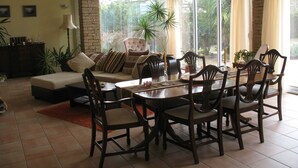 A dining area with a wooden table and chairs, a sofa, and a large window with curtains.