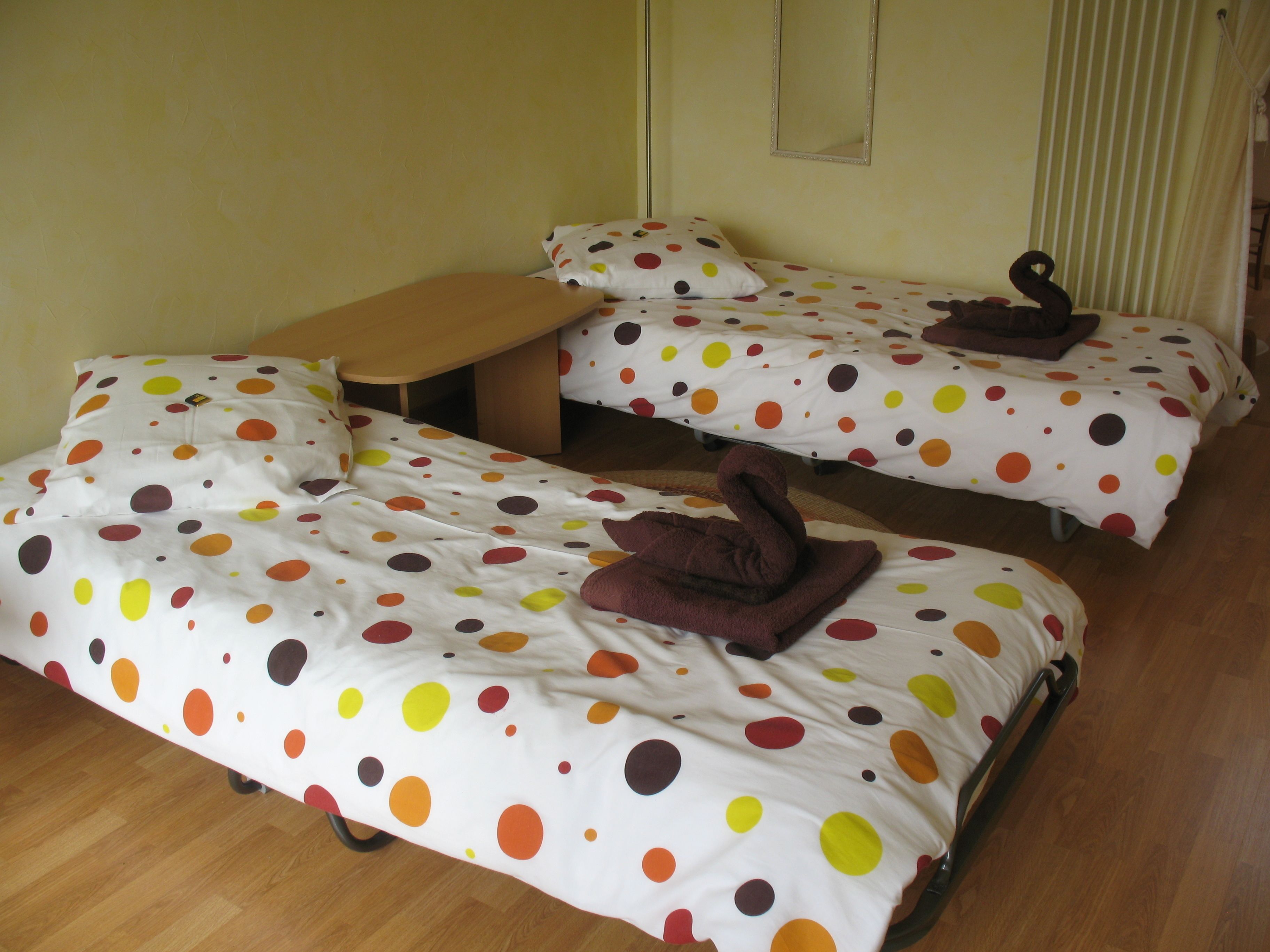 Ein Zimmer mit zwei Einzelbetten, jeweils mit Bezug in Punkteoptik, einer hölzernen Bank und einem kleinen Tisch.