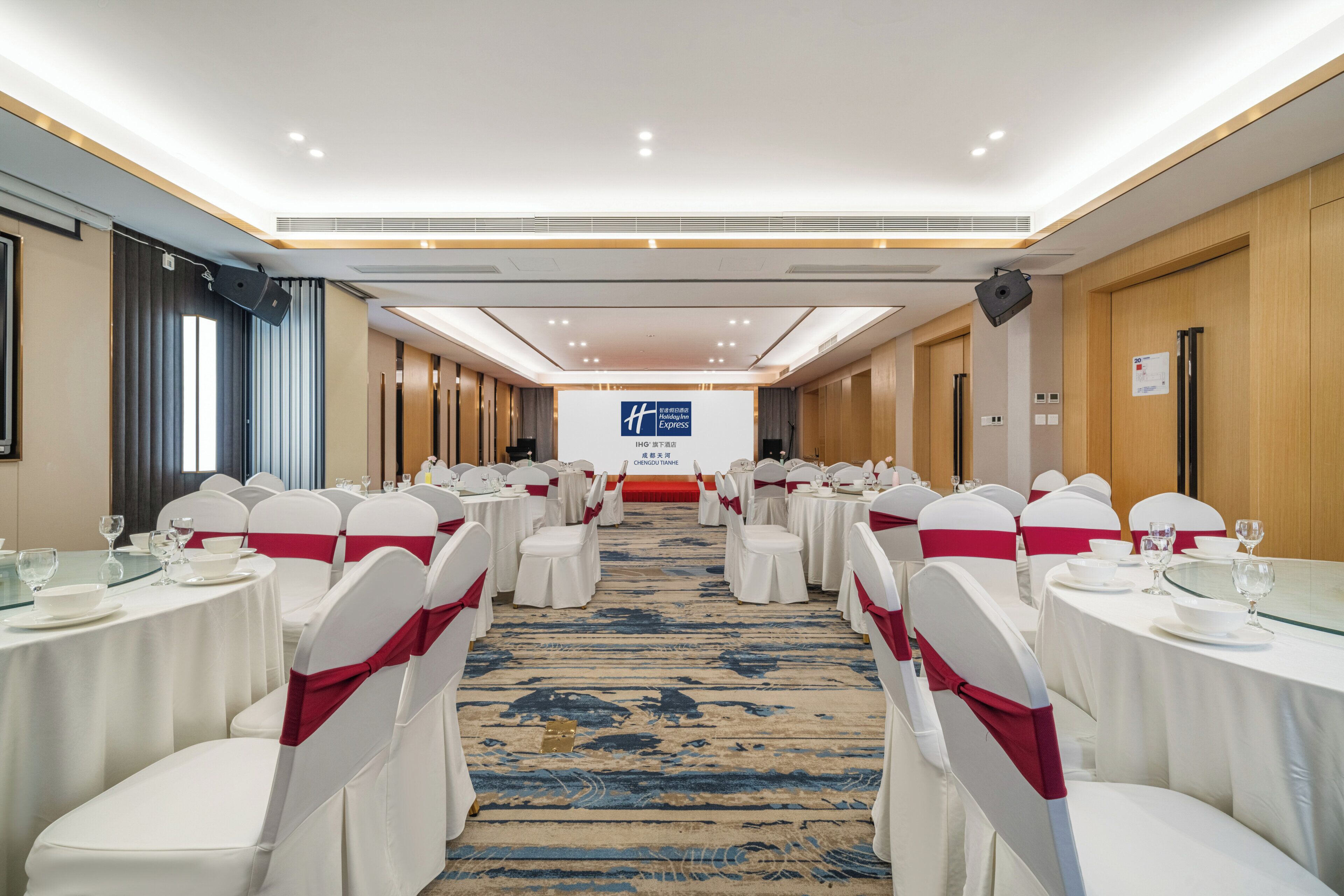 A conference room with round tables, white chairs with red sashes, and a blue carpet.