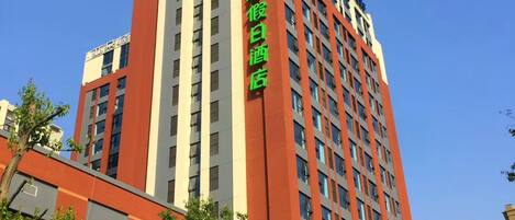 A multi-story hotel building with a prominent green sign on the facade.