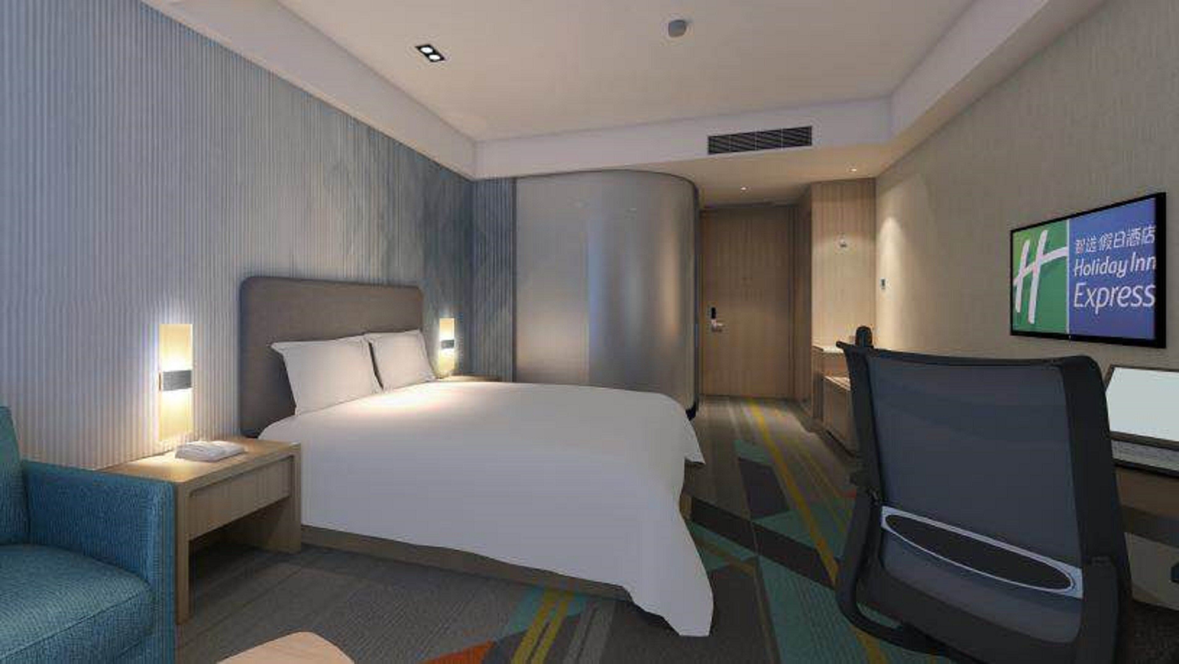 Quarto de hotel com cama, escrivaninha, cadeira, televisão e placa fixada na parede.