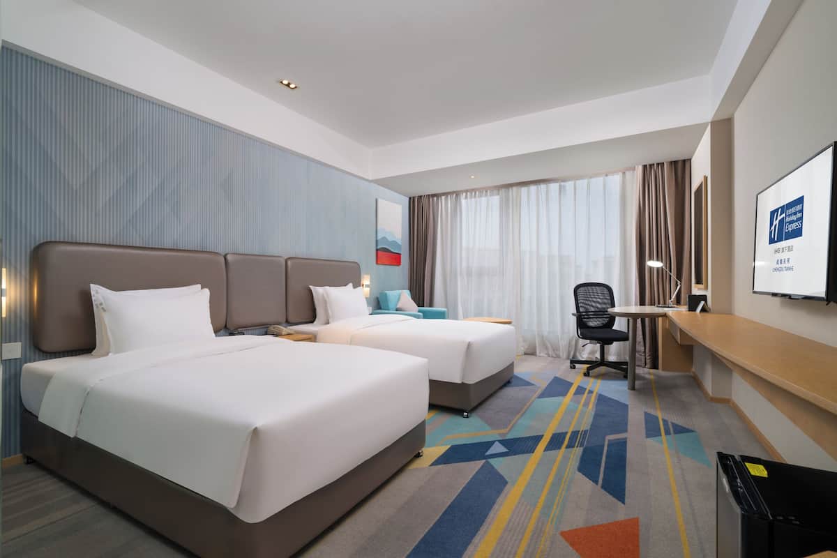 A hotel room with two beds, a desk, a chair, and a TV.