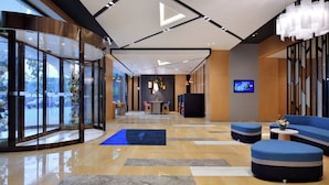 Eine moderne Lobby mit Glastür, Sitzbereichen, einer Rezeption und einem Bildschirm.