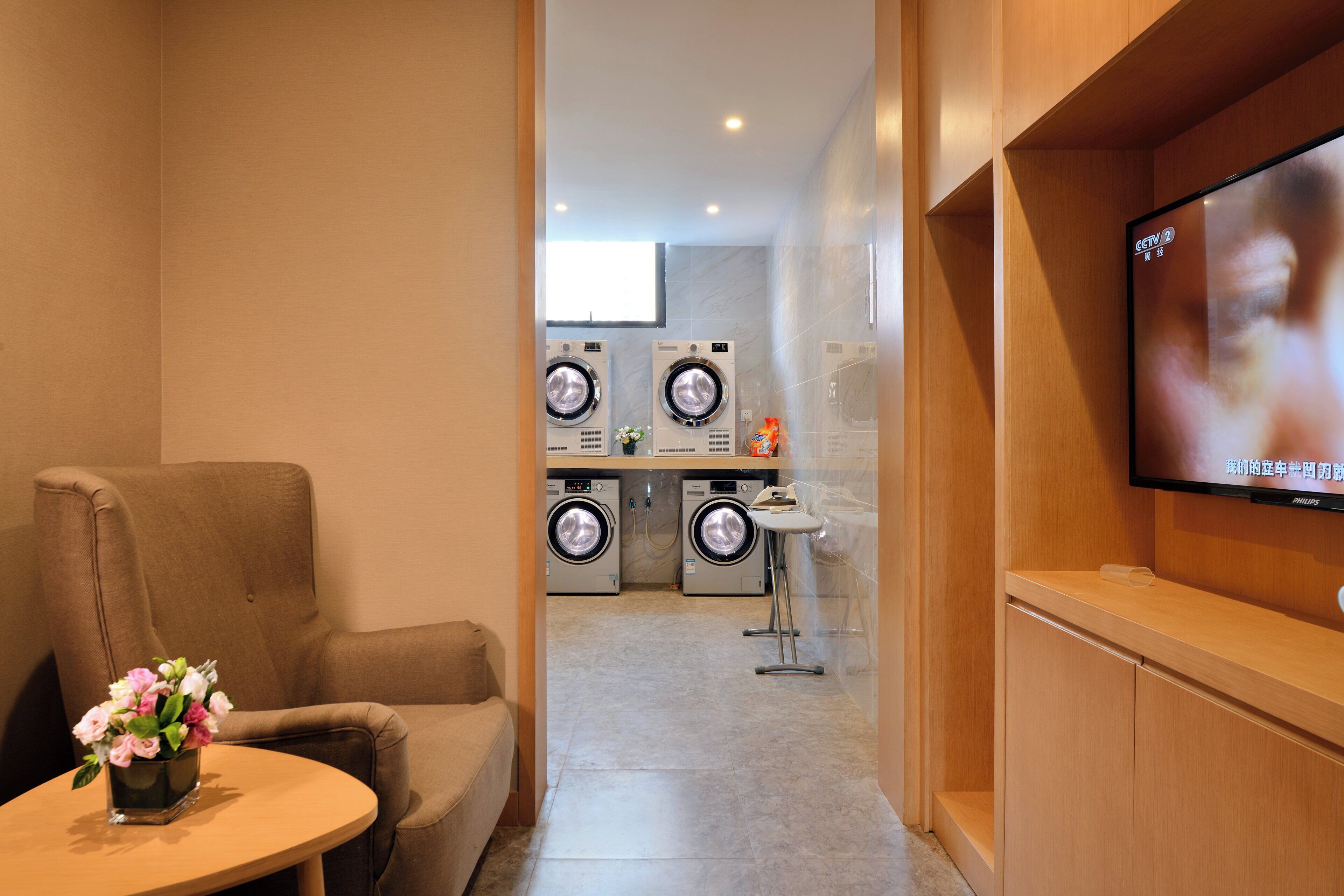 A hotel room with a sofa, a small table with a vase, a TV, and a laundry area with washers and dryers.