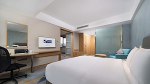 Ein Hotelzimmer mit einem großen Bett, einem Schreibtisch mit Stuhl, einem Fernseher und einer Sitzecke mit Sofa und Sesseln.