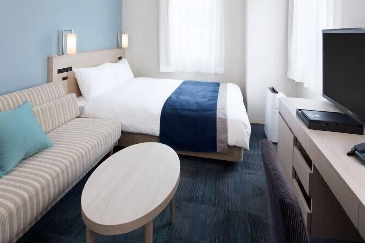 Una habitación de hotel con una cama, un sofá, una mesita, un televisor y un escritorio.