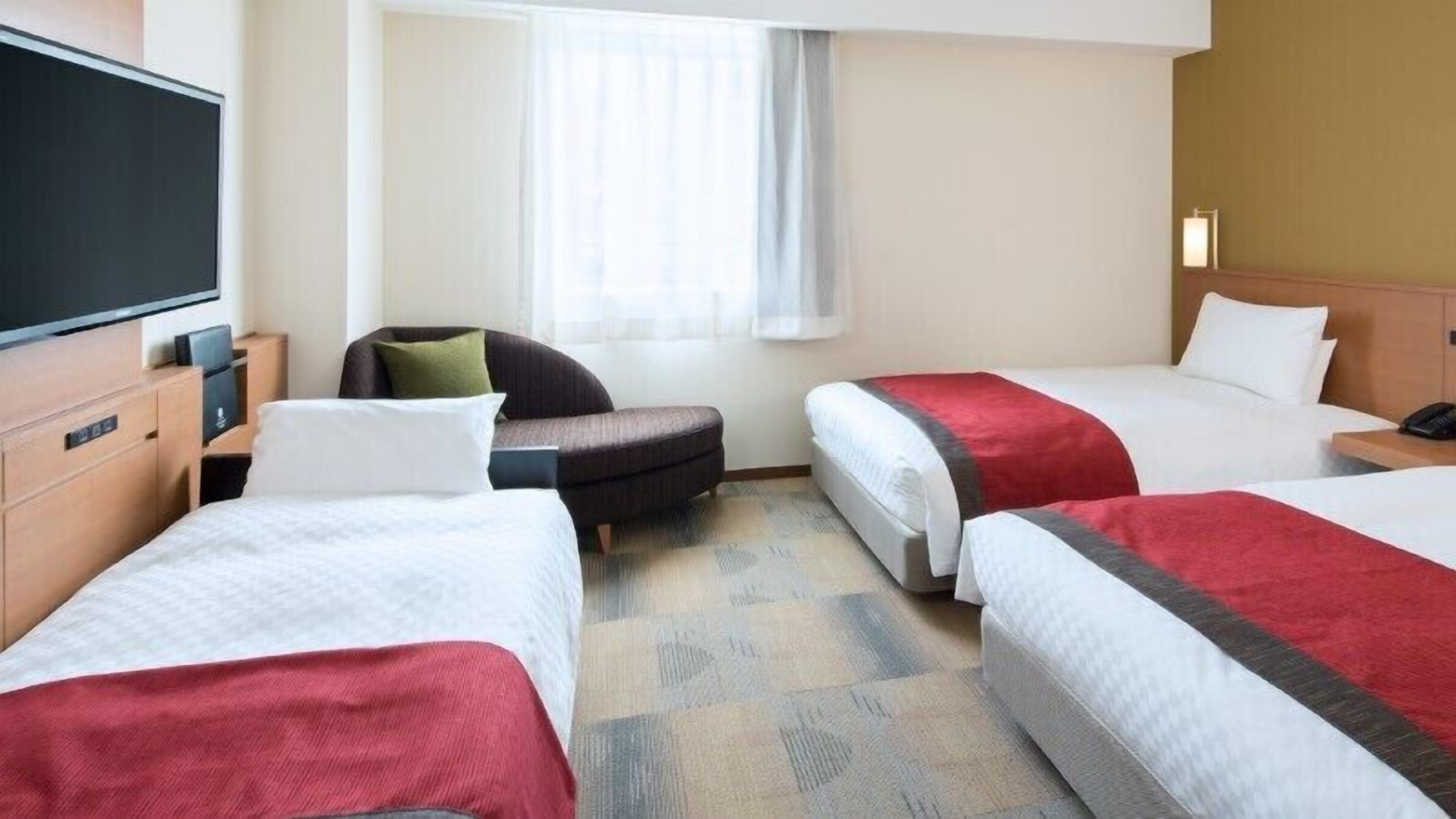 Quarto de hotel com duas camas, um sofá, uma televisão e uma janela com cortinas.