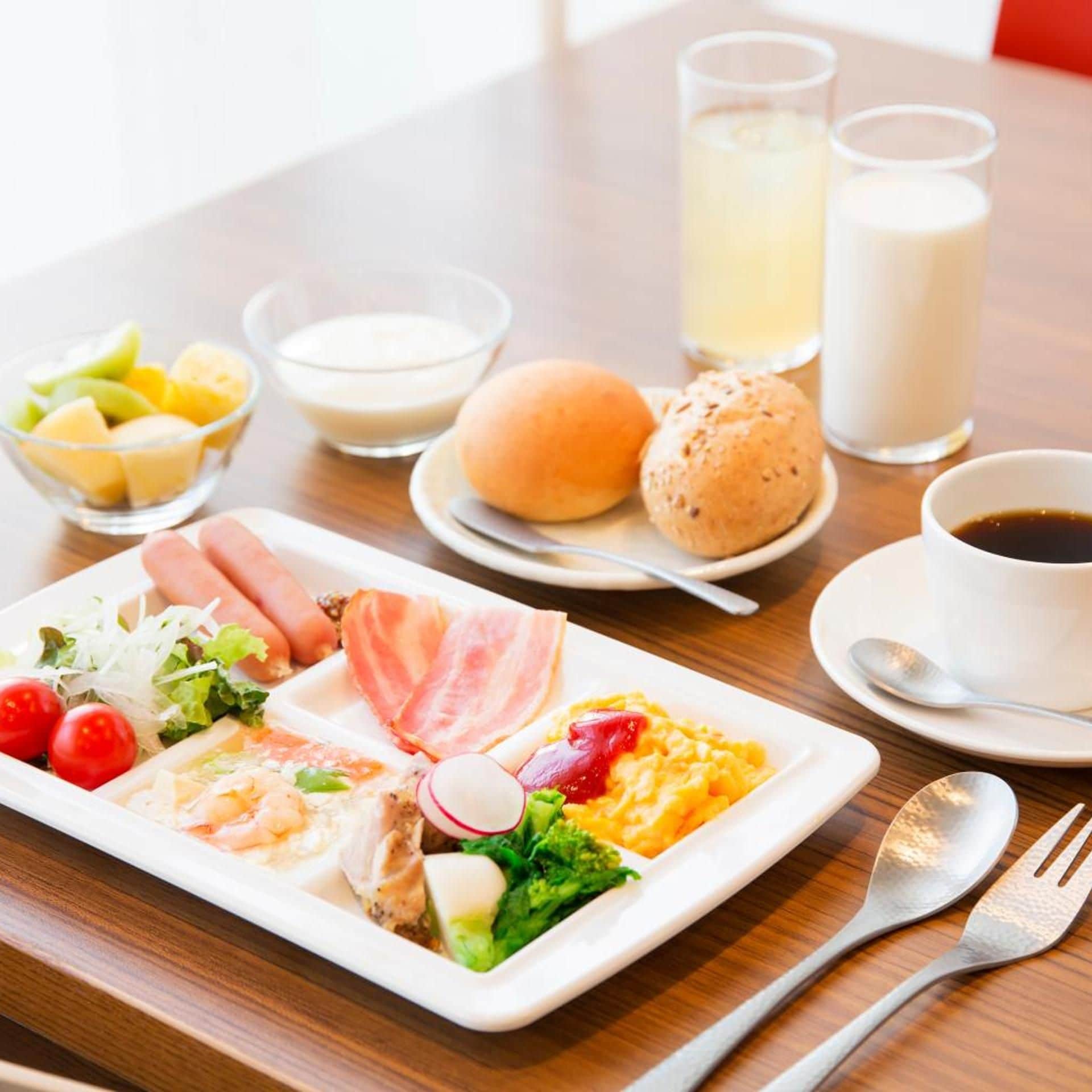 A meal with various dishes including eggs, meat, and vegetables, accompanied by drinks and bread on a table.