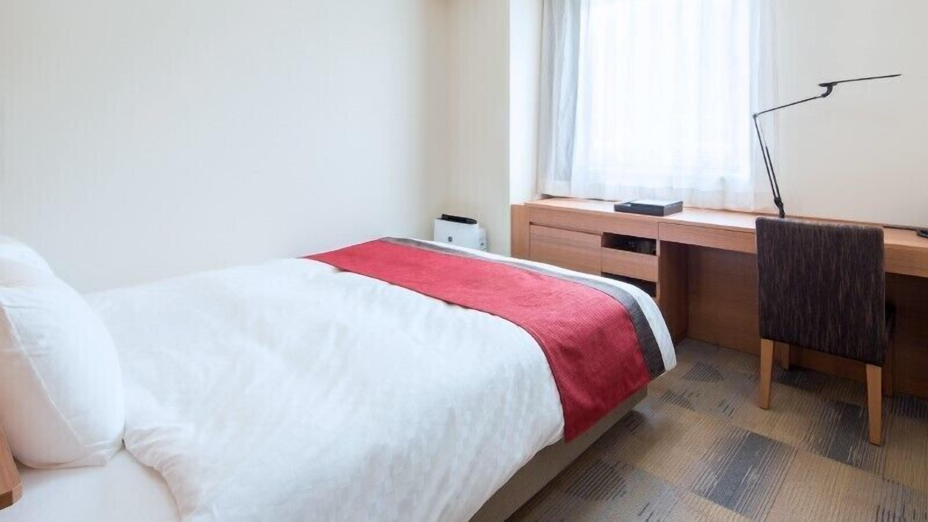 Hotellihuone, jossa on sänky, työpöytä, tuoli ja ikkuna, jossa on verhot.