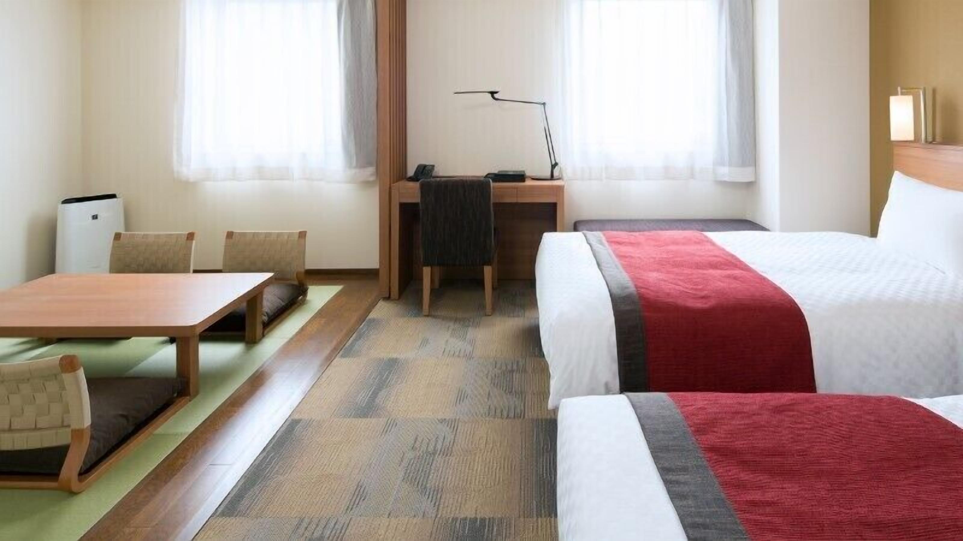 Hotellihuone, jossa on kaksi sänkyä, työpöytä, tuoli, pöytä ja lamppu.