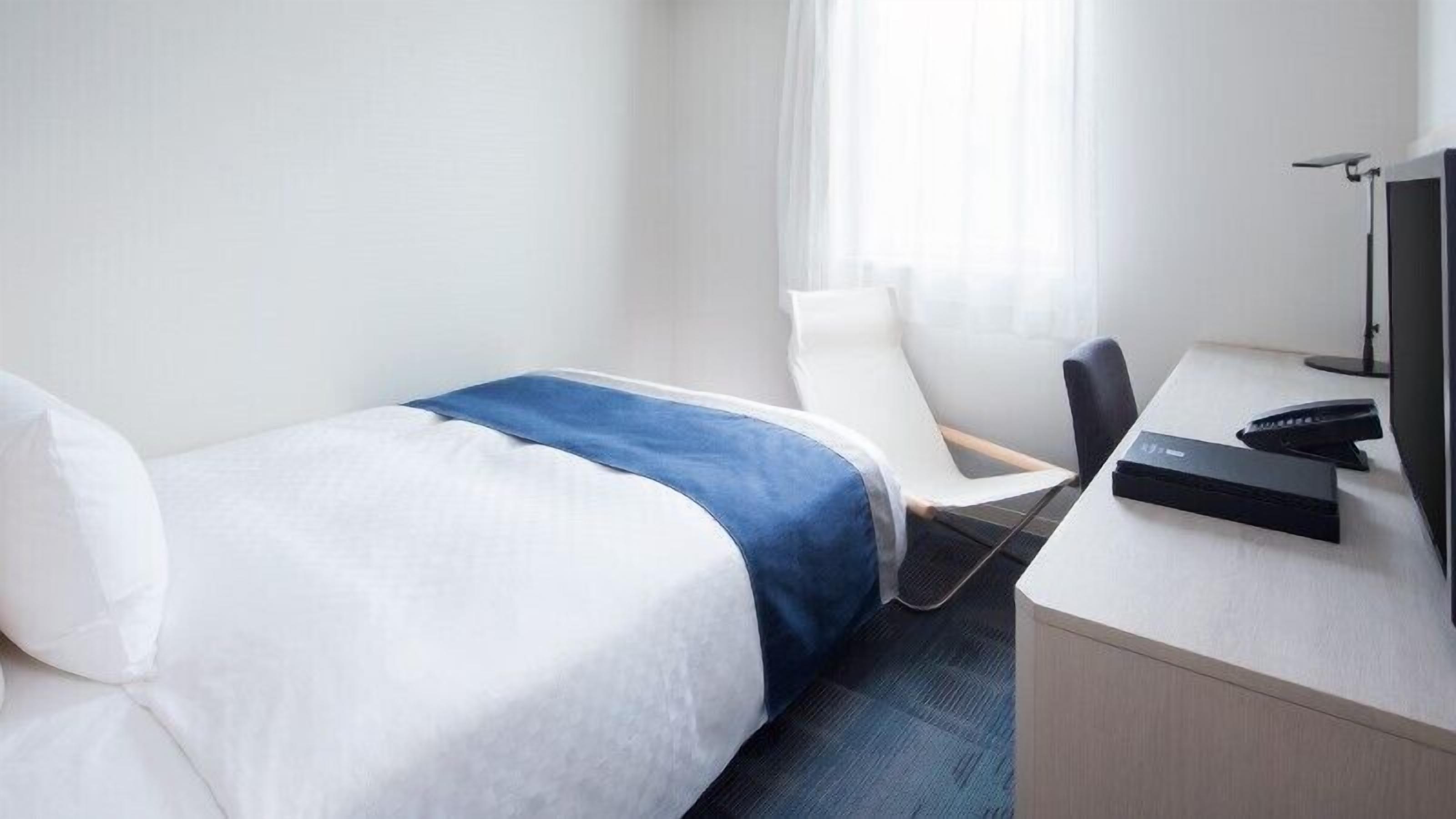Quarto de hotel com uma cama, uma escrivaninha com computador e uma cadeira.