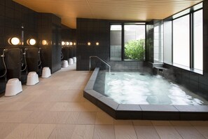Un'area spa moderna con vasca idromassaggio, diverse doccette e vista sul verde circostante.